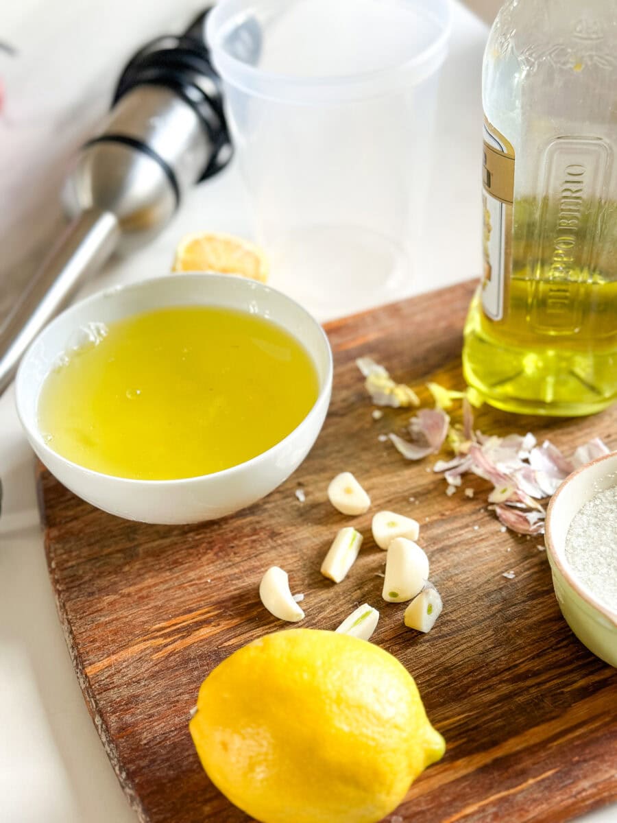 ingrédients sur planche de bois: blancs d'oeuf, huile, citron, ail, sel et pied mélangeur