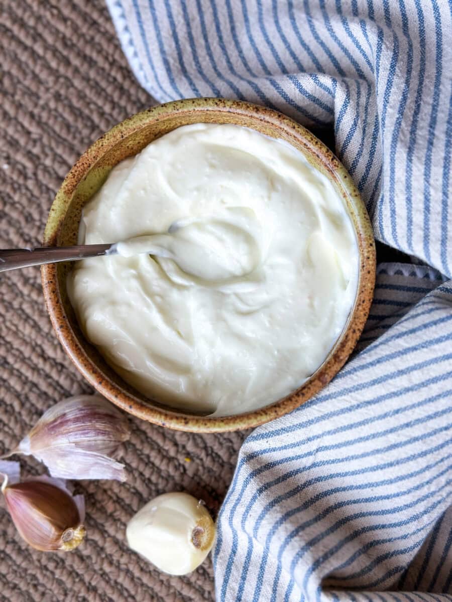 sauce à l'ail (toum) dans un petit bol avec linge de table ligné et gousses d'ail