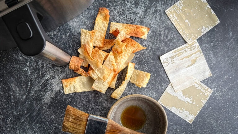 chips de wonton grillée devant tiroir du air fryer avec pâte wonton et pinceau à pâtisserie sur surface béton foncé