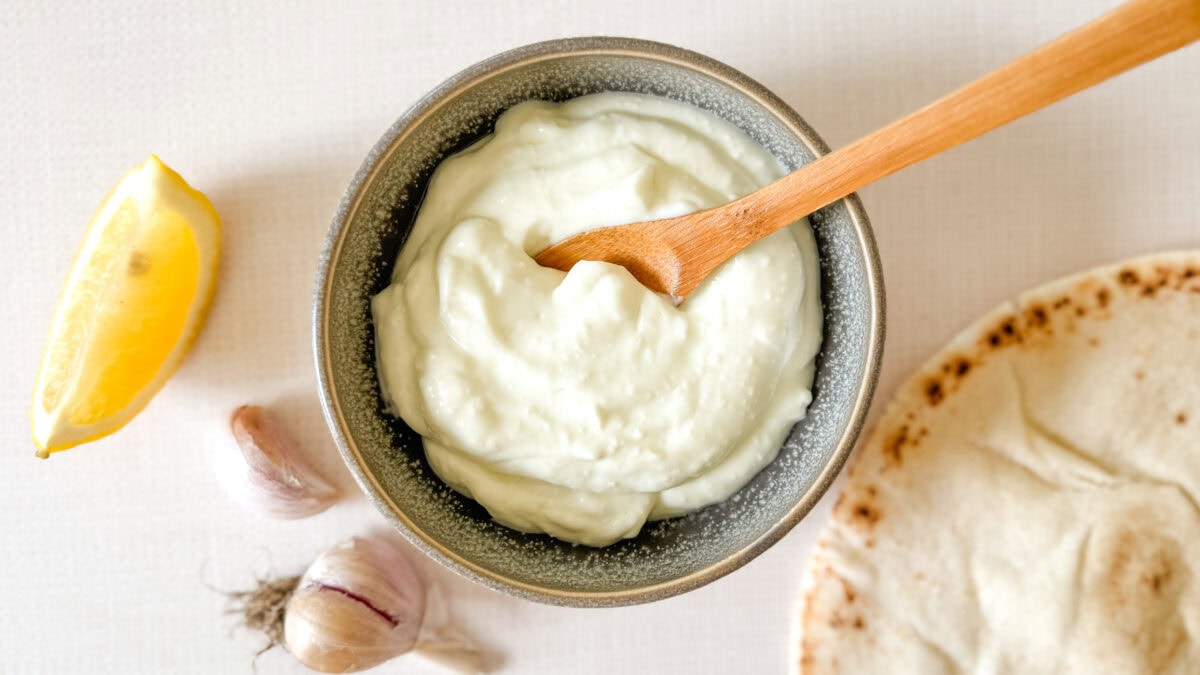 sauce à l'ail dans un petit bol avec cuillère en bois, avec gousses d'ail, citron et pain pita à côté